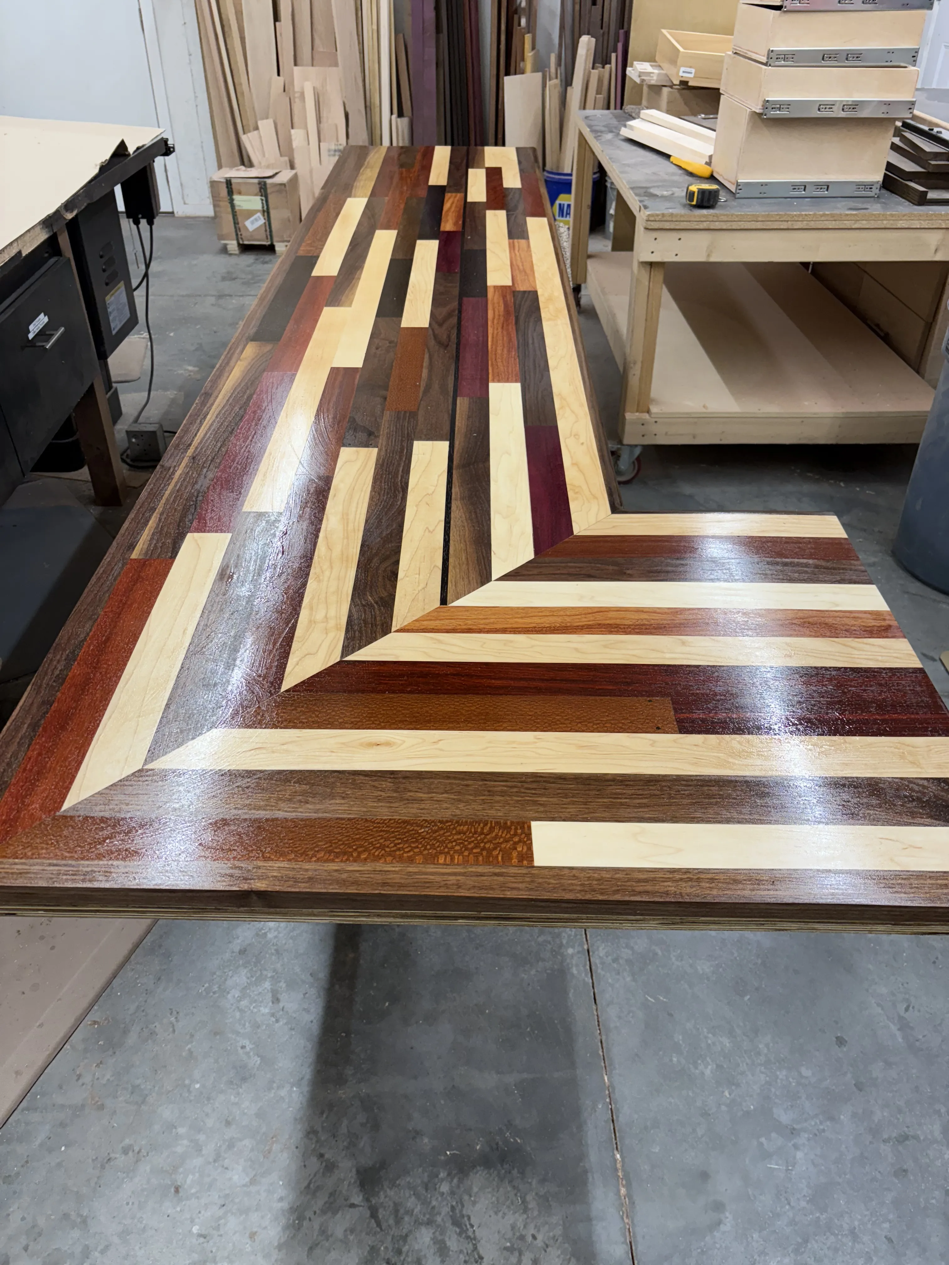 Custom wood table with a patterned mix of wood types in a woodworking workshop.